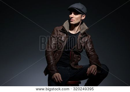 side view of a charismatic young man casually dressed sitting and looking away carefreely with a strong attitude on gray studio background