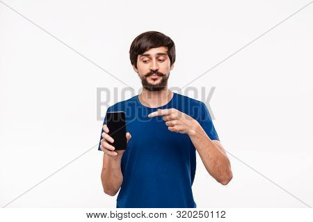 Handsome Brunet Man In A Blue Shirt With Beard And Mostaches Pointing At The Smartphone Standing Iso