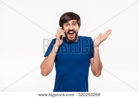 Pretty Brunet Man In A Blue Shirt With Beard And Mostaches Shocked Holding Smartphone Looking At The