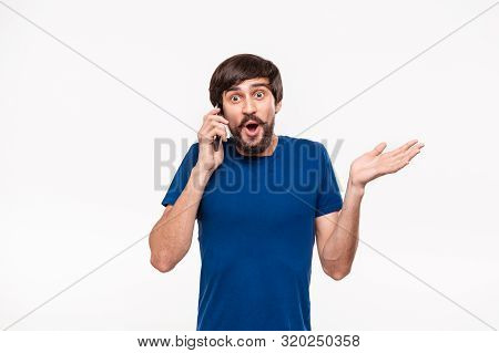 Pretty Brunet Man In A Blue Shirt With Beard And Mostaches Shocked Holding Smartphone Looking At The