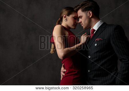 side view of a young sexy couple strongly embracing one another and looking with passion and desire on gray studio background