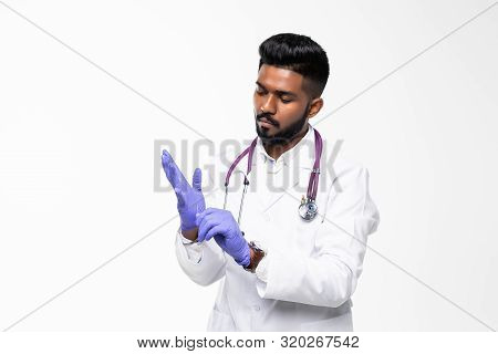 Indian Doctor Or Physician Male Looking At Hand With Focused Expression As Putting On Blue Surgical 