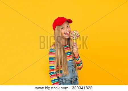 Lollipop Makes Her Happy. Cute Little Girl Eating Rainbow Swirl Candy On Yellow Background. Small Ch