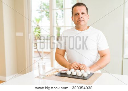 Middle age man eating asian dumplings at home with serious expression on face. Simple and natural looking at the camera.