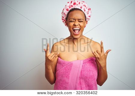 African american woman wearing pink shower towel after bath over isolated background shouting with crazy expression doing rock symbol with hands up. Music star. Heavy concept.