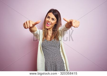 Young beautiful woman standing over pink isolated background approving doing positive gesture with hand, thumbs up smiling and happy for success. Winner gesture.