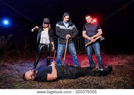 Three Bandits Near Dead Man In The Field At Night. Photoshoot About Life Of Gungsters In Russia