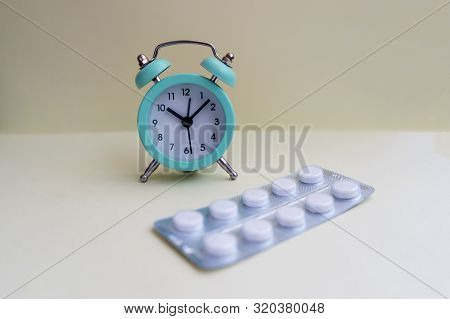 Pills Lie Next To The Alarm Clock On A Light Background. Healthcare And Medicine Concept.