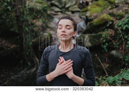 Young Woman Practicing Breathing Yoga Pranayama Outdoors In Moss Forest On Background Of Waterfall. 