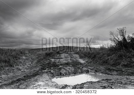 Dirt Road After Heavy Rain Leading To The Top Of The Hill, Stormclouds On The Dark Sky In Black And 