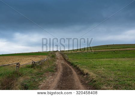 Dirt Road After Heavy Rain Leading To The Top Of The Hill, Stormclouds On The Dark Sky.