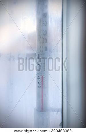 View Through Frozen Window To Outdoor Thermometer Which Showing Subzero Temperature.