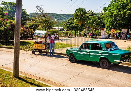Santiago De Cuba, Cuba - 2019. Cuban Selling Homemade Juice In Front Of A Vintage American Car.