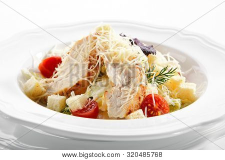 Macro shot of caesar salad with roasted chicken breast, croutons, cherry tomatoes and grated parmesan cheese on white plate. Delicious restaurant starter menu with barbecue meat salat closeup