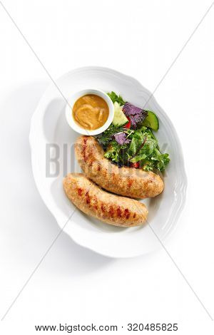 Top view of Bavarian sausages for frying with mustard sauce and mixed salad isolated. Traditional German rostbratwurst, wurst or bratwurst with fresh lettuce, rucola and chard leaves topview