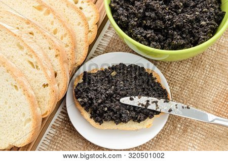 Tapenade Sandwich And Table Knife On A Sauser, Green Bowl With Fresh Tapenade And Sliced Wheat Bread
