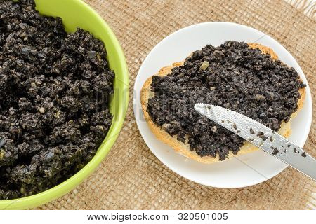 Fresh Tapenade In A Green Bowl, Tapenade Sandwich With Slice Of Wheat Bread And Table Knife On A Sau