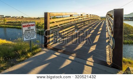 Panorama Warning Sign And Bridge Over A Lake Sourrounded By Houses And Grassy Terrrain