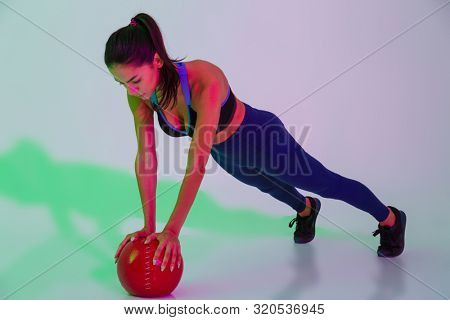 Photo of concentrated young fitness woman isolated with led flash lights make exercises with ball.
