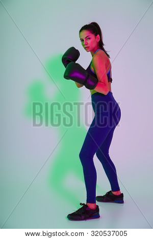 Image of young amazing beautiful strong fitness woman boxer isolated with led flash lights make boxing exercises in gloves.