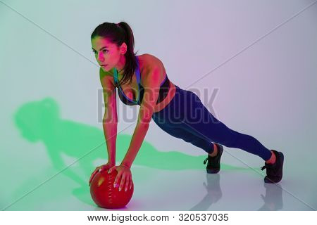 Image of serious young fitness woman isolated with led flash lights make exercises with ball.