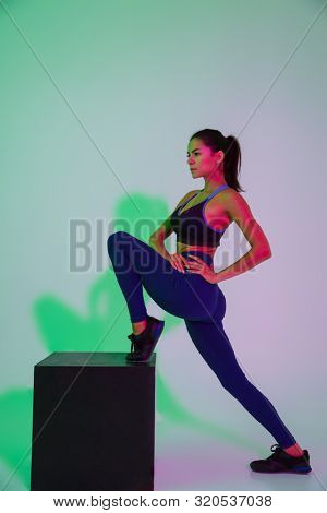 Picture of serious beautiful young sports woman posing isolated with led flash lights make stretching exercises.