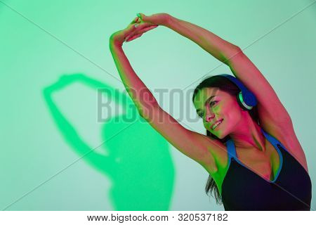 Image of happy cheery young strong fitness woman make stretching exercise isolated with led flash lights listening music with headphones.