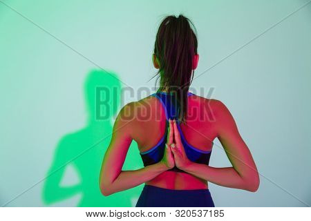 Back view image of young sports woman posing isolated with led flash lights make stretching exercise for arms.