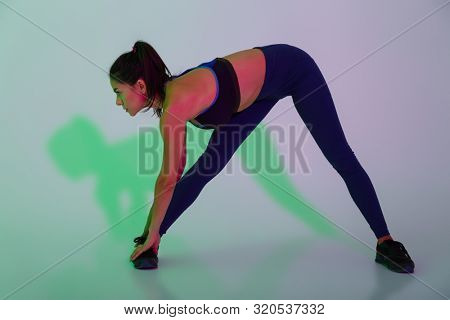 Photo of a concentrated young sports woman posing isolated with led flash lights make stretching exercises.