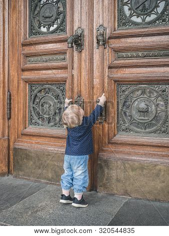 A Little Girl, Standing On Tiptoe, Reaches Out To The Massive Doors Of The University, Trying To Ope