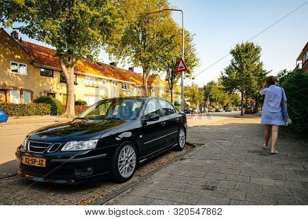 Haarlem, Netherlands - Aug 26, 2019: Rear View Of Elegant Dutch Woman Walking Near Black Luxury Saab