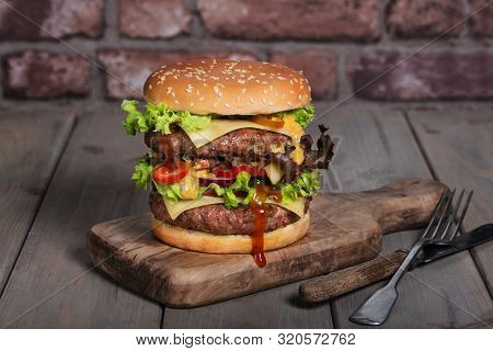 Hamburger With A Double Serving Of Meat, Tomatoes, Salad, Onions On A Wooden Board In A Restaurant.c