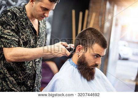 Making Haircut Look Perfect. Young Bearded Man Getting Haircut By Hairdresser While Sitting In Chair