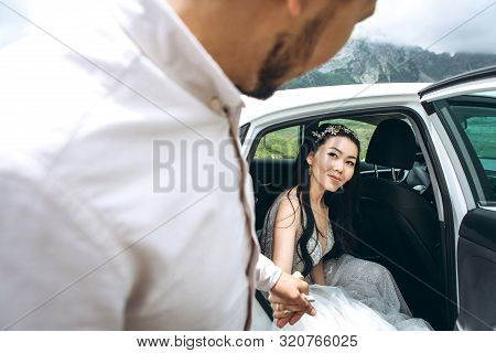 The Groom Or Husband Helps His Bride Or Wife To Get Out Of The Car. They Are Going To Get Married Or