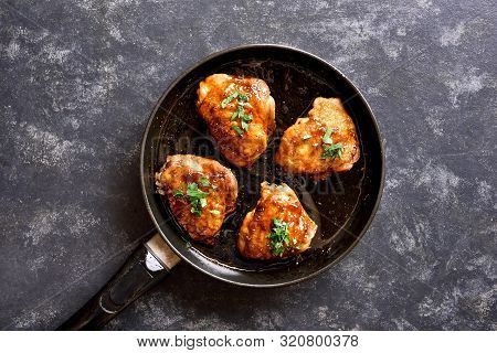 Sweet And Spicy Honey Grilled Chicken Thighs In Frying Pan Over Dark Stone Background. Tasty Food In