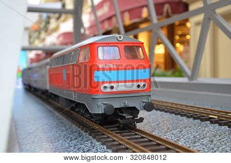 Miniature Red Toy Train With A Blue Stripe On Rails On A Railway Bridge