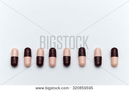 Prescription Drugs, Capsules Of Soft Pink And Dark Reddish Brown Colors All Mixed In. On White Backg