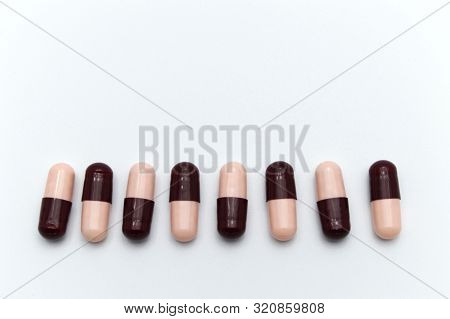 Prescription Drugs, Capsules Of Soft Pink And Dark Reddish Brown Colors All Mixed In. On White Backg