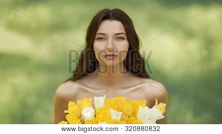 Attractive Woman In Red Dress With A Bouquet Of Spring Flowers Against Nature Bokeh Green Background