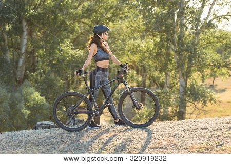 Girl On A Mountain Bike On Offroad, Beautiful Portrait Of A Cyclist At Sunset, Fitness Girl Rides A 