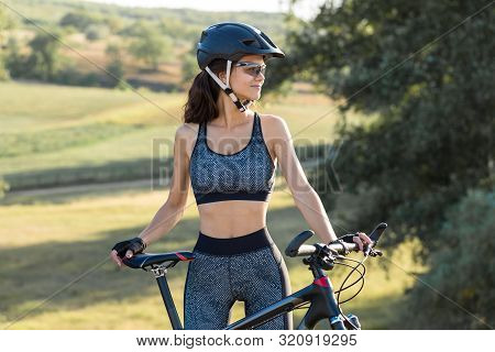 Girl On A Mountain Bike On Offroad, Beautiful Portrait Of A Cyclist At Sunset, Fitness Girl Rides A 