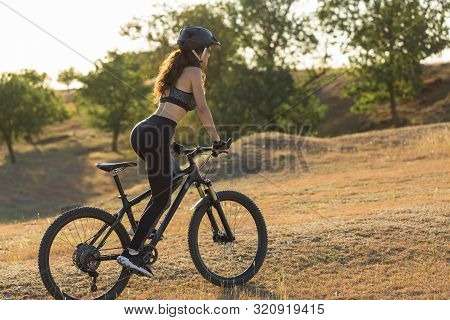 Girl On A Mountain Bike On Offroad, Beautiful Portrait Of A Cyclist At Sunset, Fitness Girl Rides A 