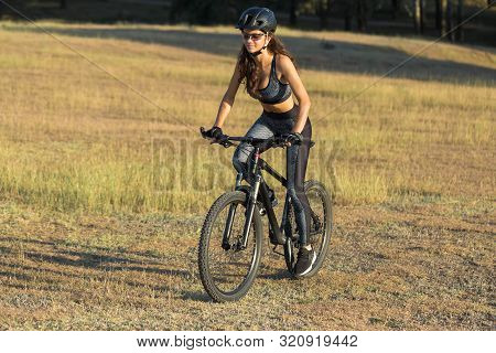 Girl On A Mountain Bike On Offroad, Beautiful Portrait Of A Cyclist At Sunset, Fitness Girl Rides A 