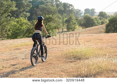 Girl On A Mountain Bike On Offroad, Beautiful Portrait Of A Cyclist At Sunset, Fitness Girl Rides A 