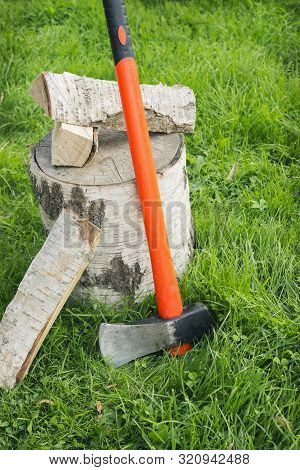 Stump With An Splitting Axe And Firewood On The Grass. Birch Logs
