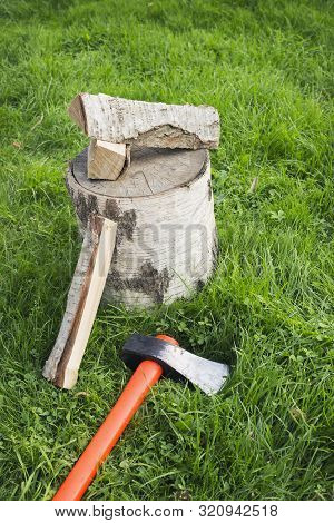 Stump With An Splitting Axe And Firewood On The Grass. Birch Logs