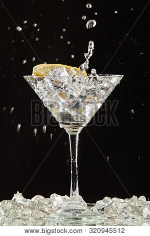 Glass Of Water, Lemon And Watersplashes On A Black Studio Background