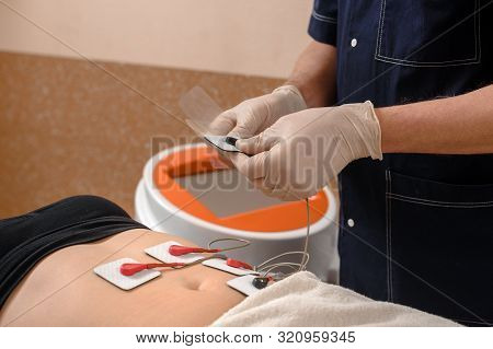 Closeup Of Professional Cosmetologist Doing Myostimulation Procedure On Belly For Female Client