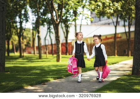 Portrait Of Happy Caucasian Young Smiling Girls Wearing School Backpack Outside The Primary School. 