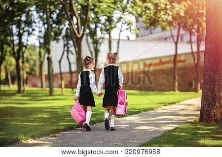 Portrait Of Happy Caucasian Young Smiling Girls Wearing School Backpack Outside The Primary School. 